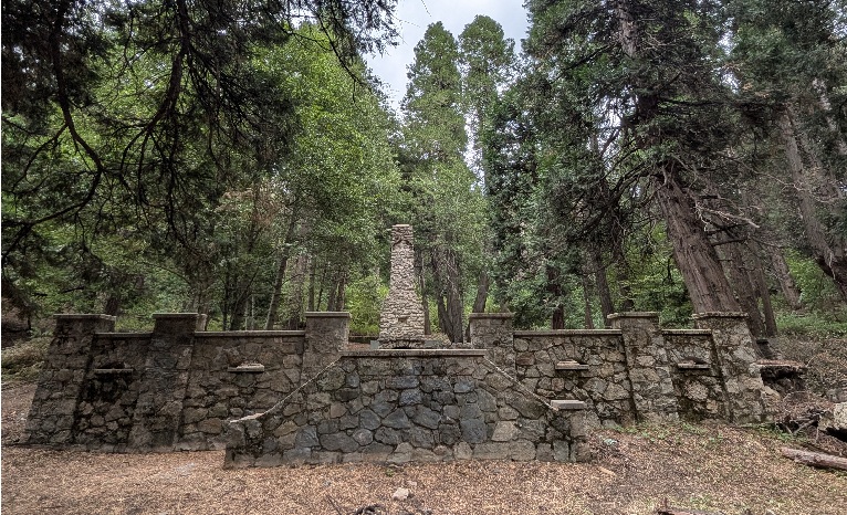 The granite wall and central chimney standing among tall pines on the property today.